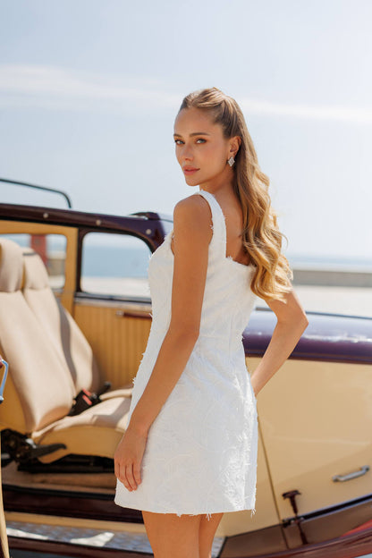 Woman in a white dress standing next to a vintage car with a clear sky background