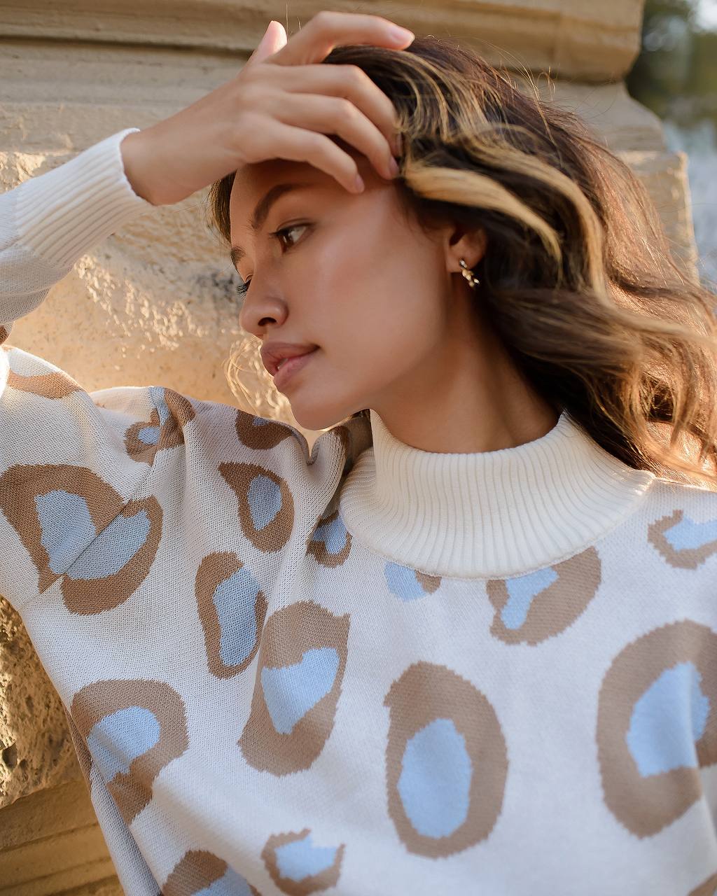 Woman wearing a white sweater with brown and blue abstract pattern, standing outdoors.