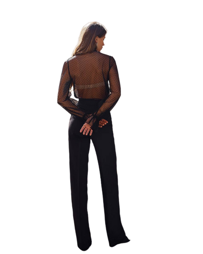 Woman wearing a sheer brown top and black pants on a white background