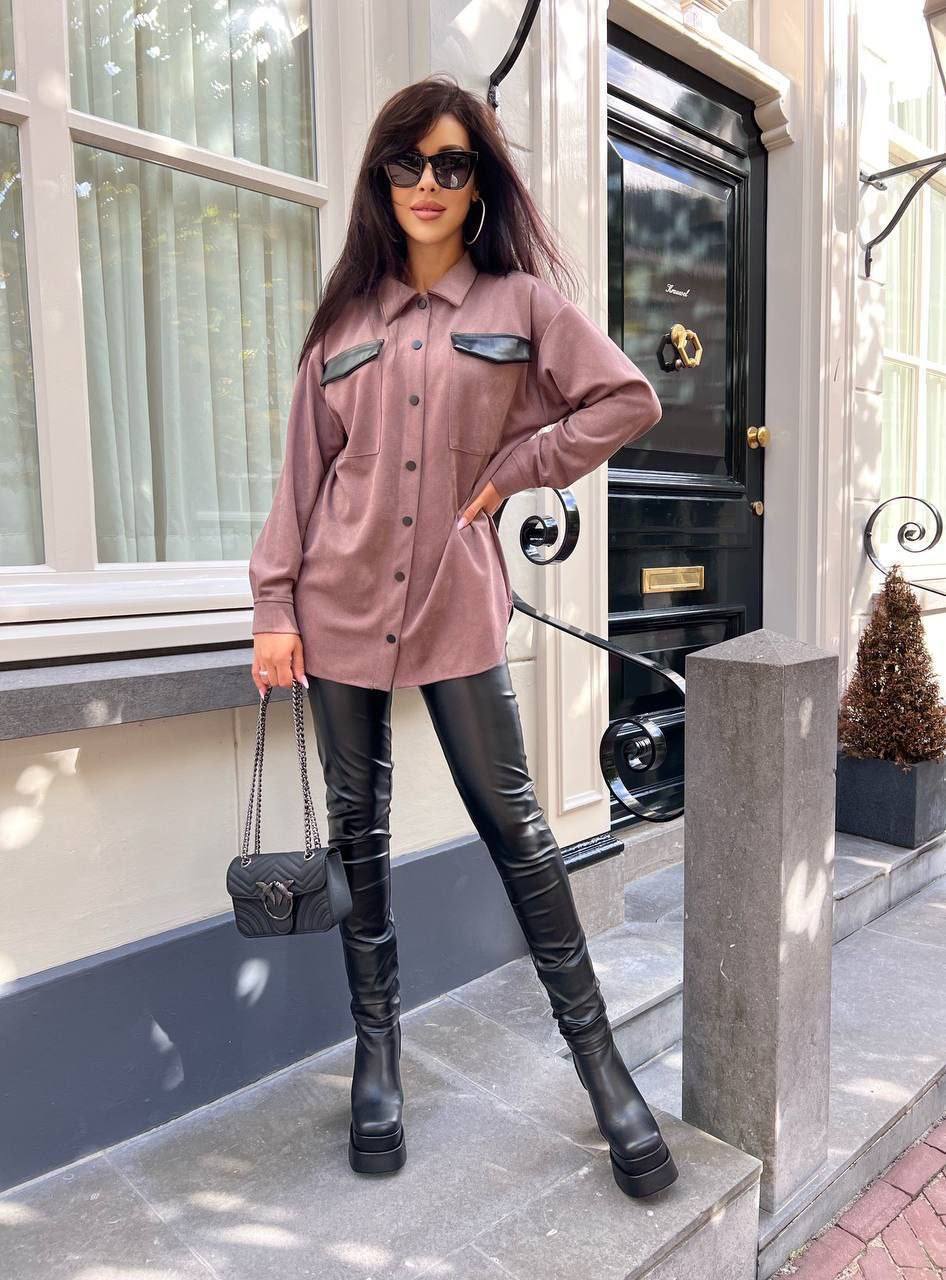 Woman in a pink shirt and black leather pants standing on steps outside a building.