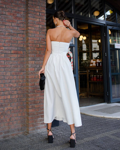Woman in a white strapless dress standing against a brick wall.