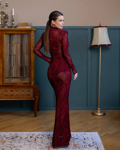 Woman in a burgundy evening gown standing in a room with wooden floor and decorative elements.