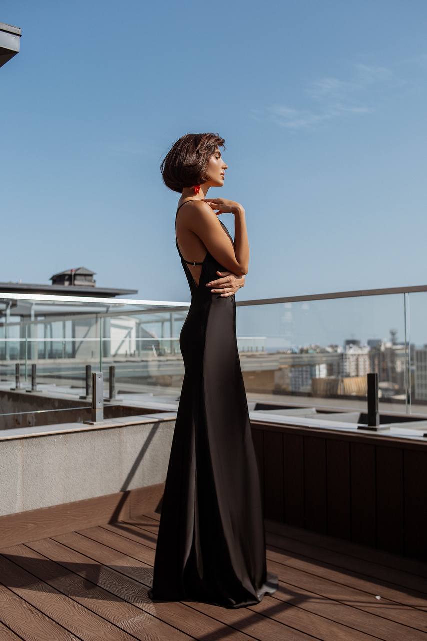 Woman in a black evening gown standing on a rooftop with a cityscape in the background