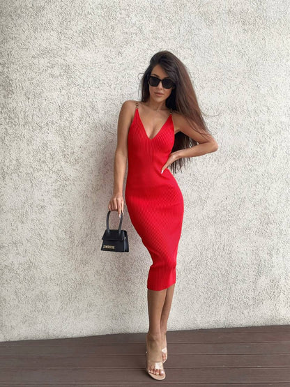 Woman in a red dress holding a black handbag against a textured wall.