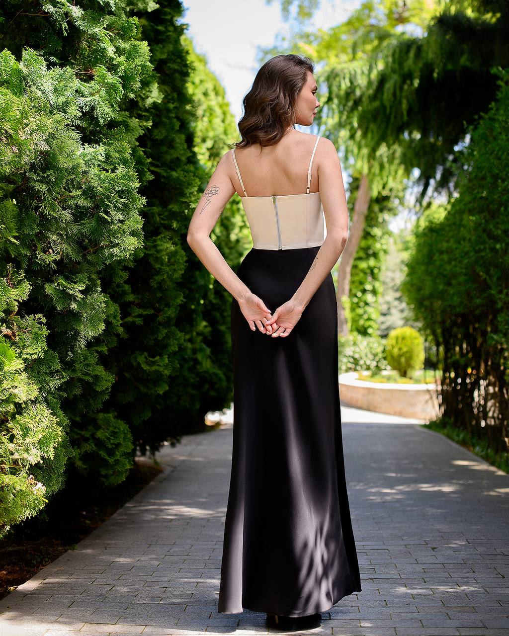 Woman in a black and beige dress standing in a garden path