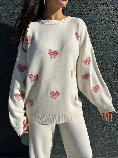 Person wearing a white sweater with red heart patterns against a dark background