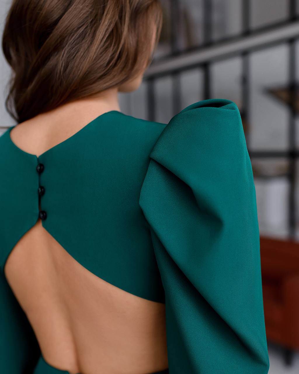 Green dress with cut-out back worn by a person, blurred indoor background