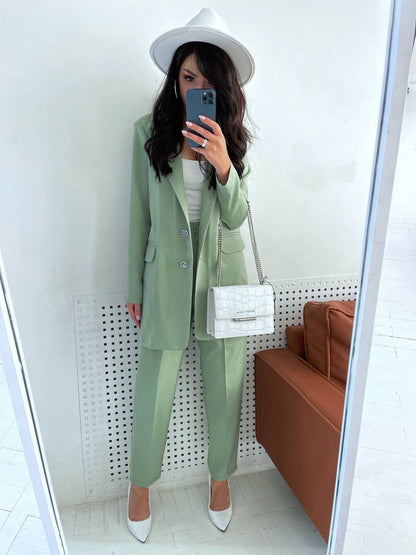 Person wearing a green suit with a white hat and shoes, holding a phone in a room with a white wall and brown couch.