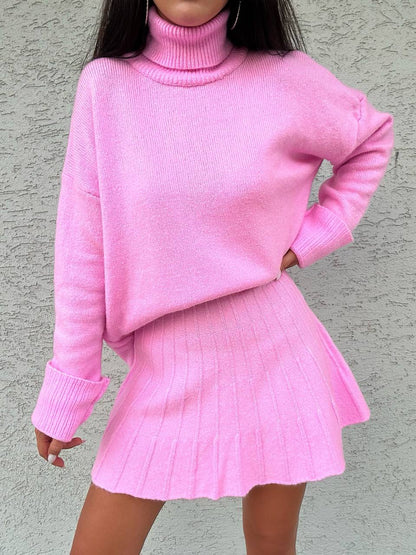 Person wearing a pink ribbed sweater and skirt set against a gray background