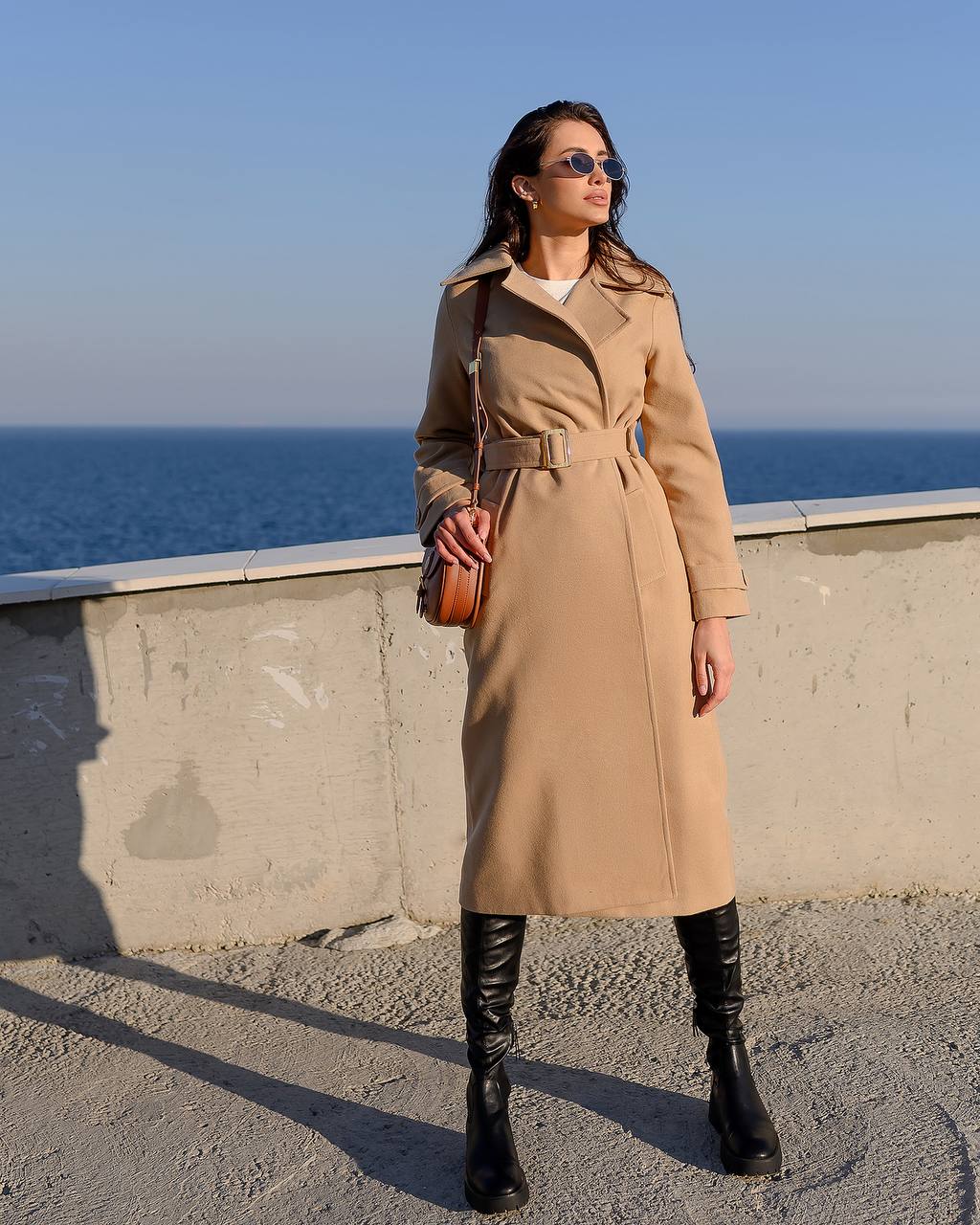 Woman in a beige coat standing by the ocean