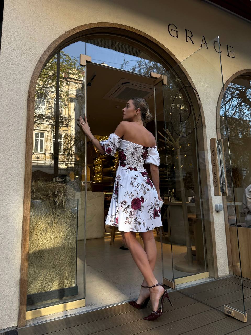 Woman in a floral dress standing outside a building with 'GRACE' on the door.