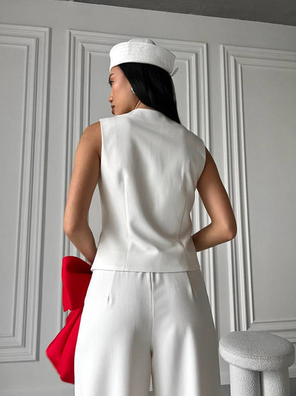 Person wearing a white outfit with a red bag against a gray paneled wall