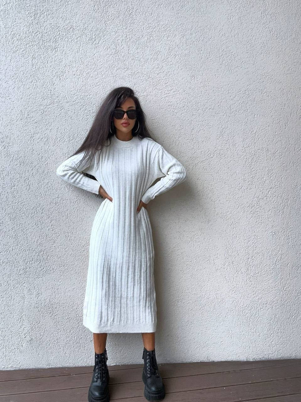 Woman wearing a white ribbed dress against a plain wall