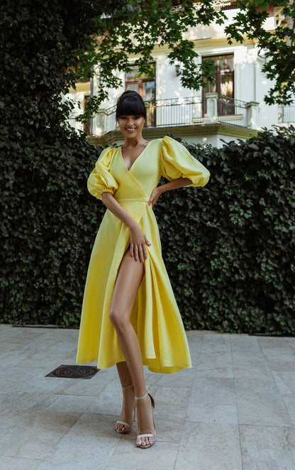 Woman in a yellow dress standing outdoors with greenery in the background