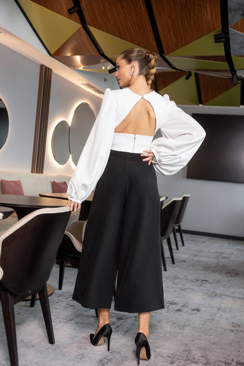 Woman in a white blouse with open back and black pants standing in a modern restaurant.