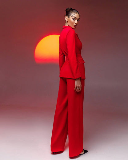Woman in a red suit standing against a gradient background with a sun-like shape.