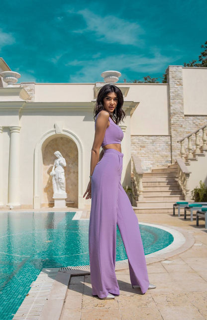 Woman in a purple outfit standing by a pool with classical architecture in the background