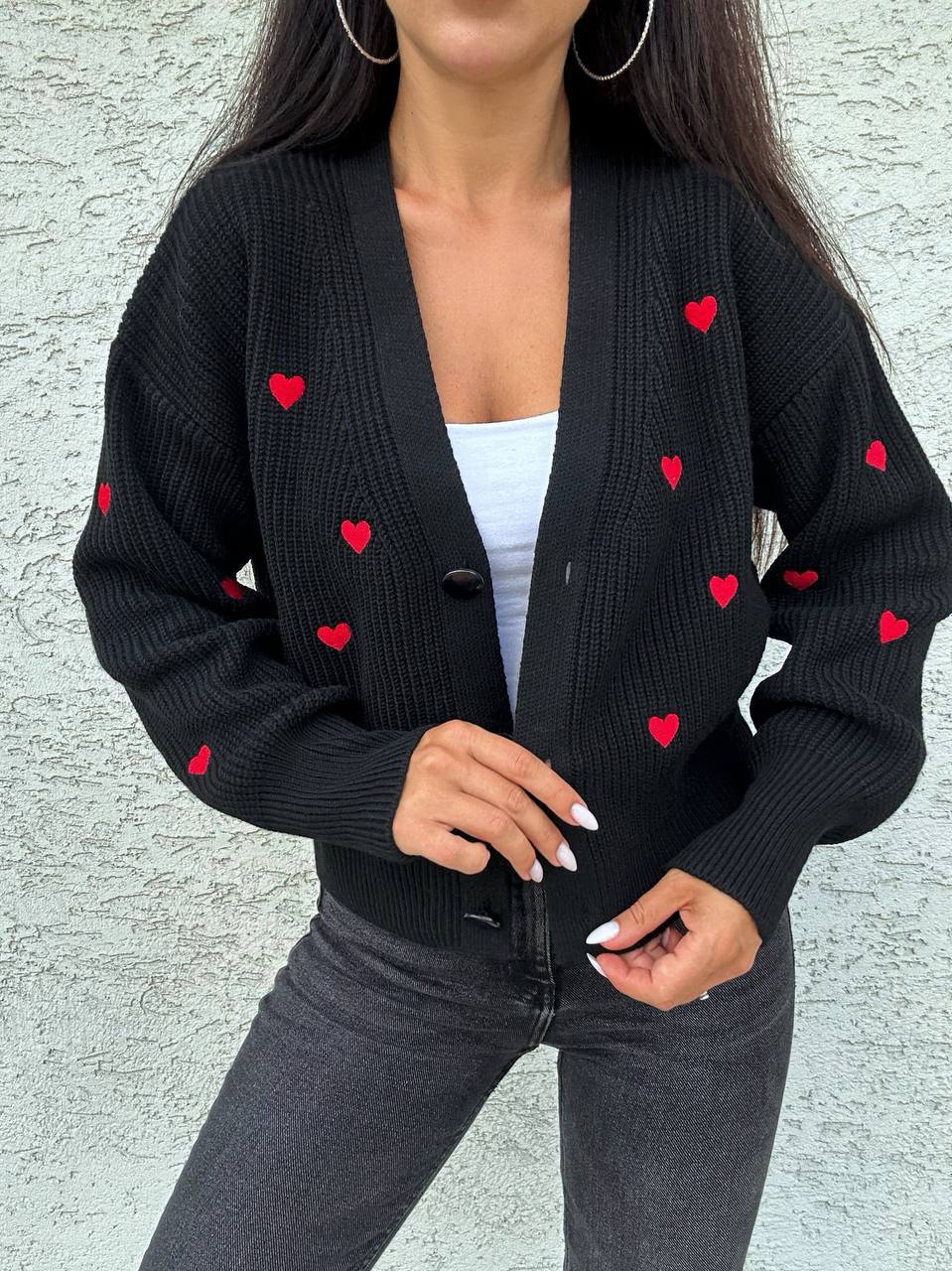 Black cardigan with red heart patterns worn by a person against a light gray background