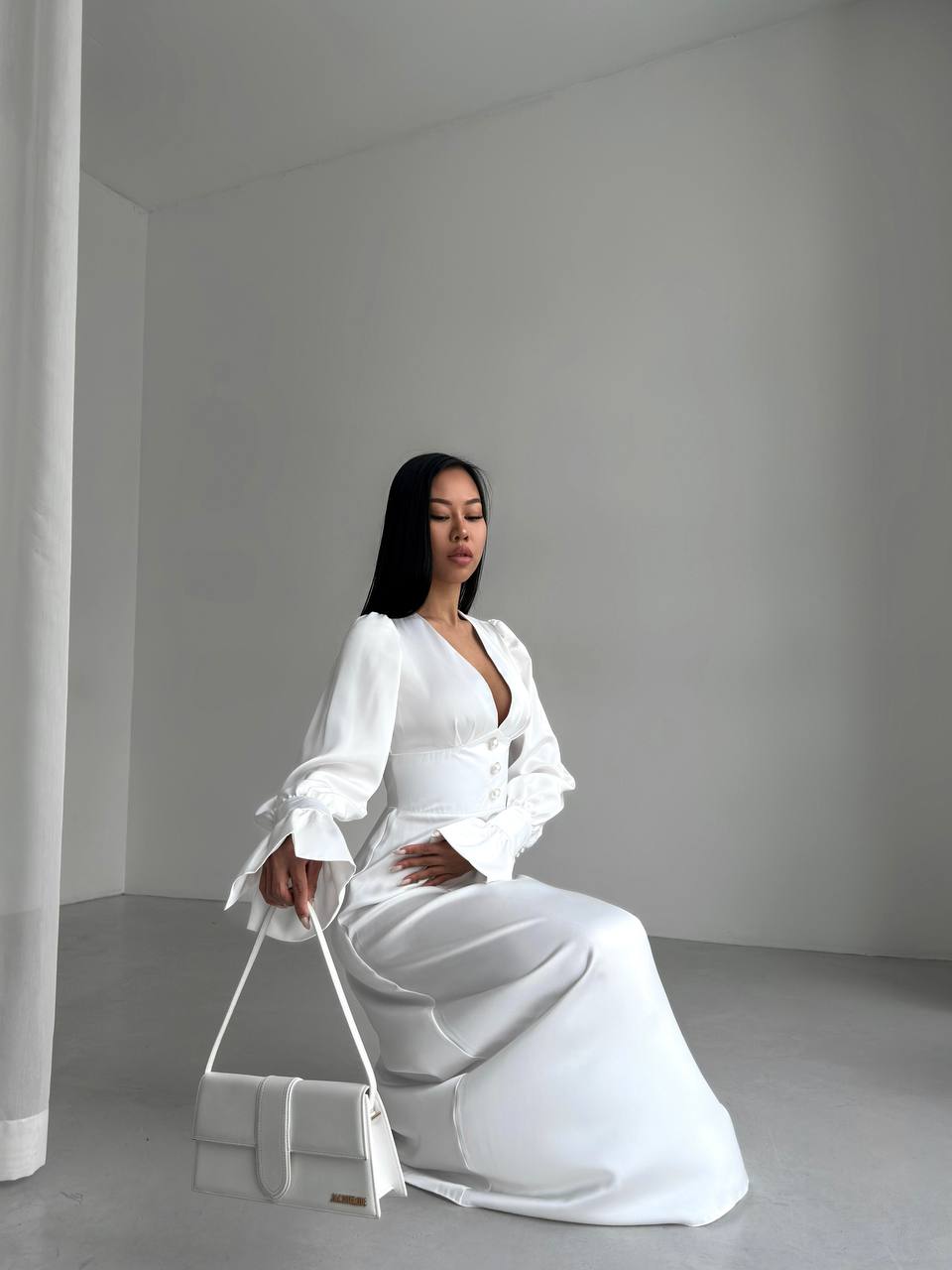 Woman in a white outfit sitting on a white stool against a plain background