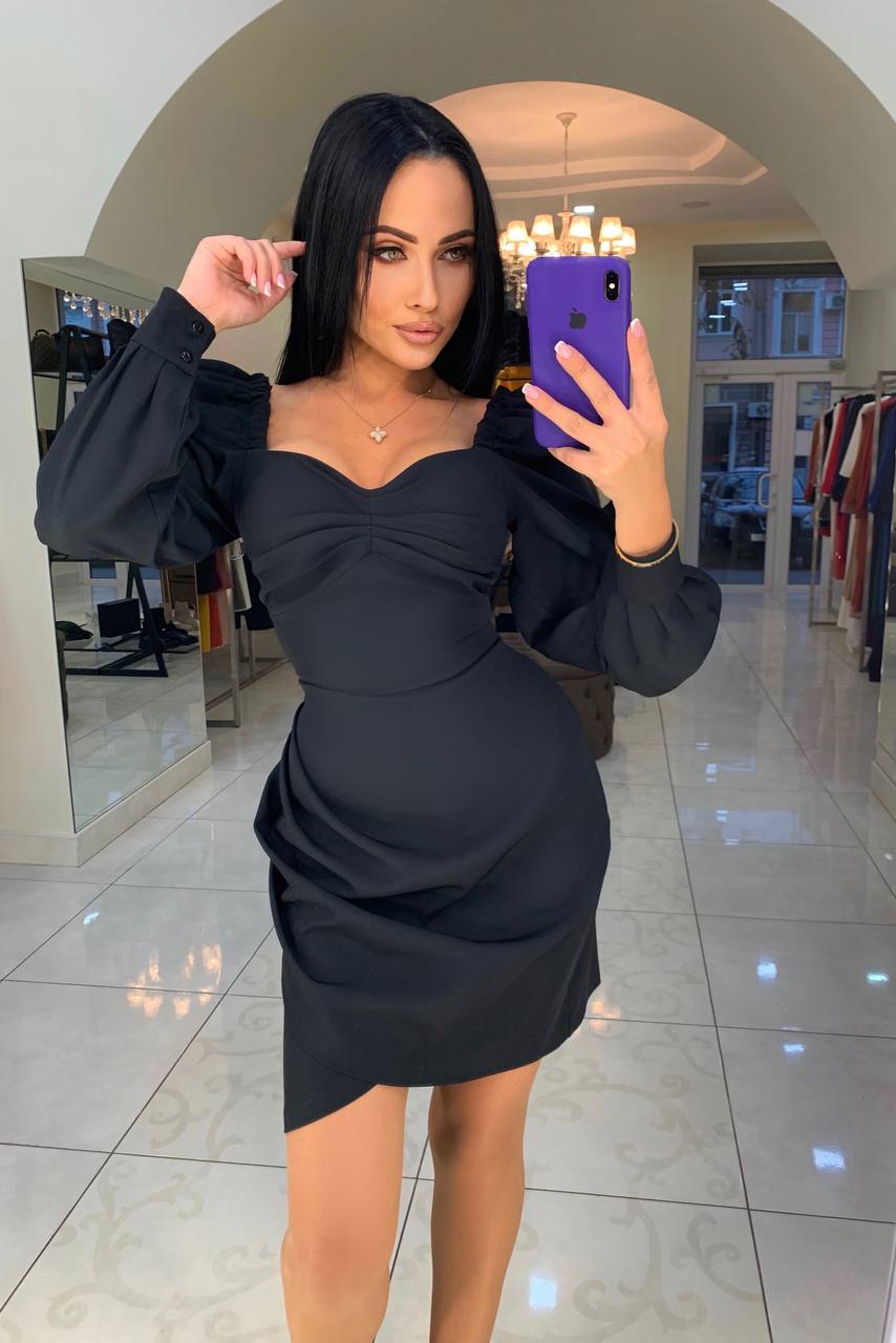 Woman taking a mirror selfie wearing a black dress in a store.