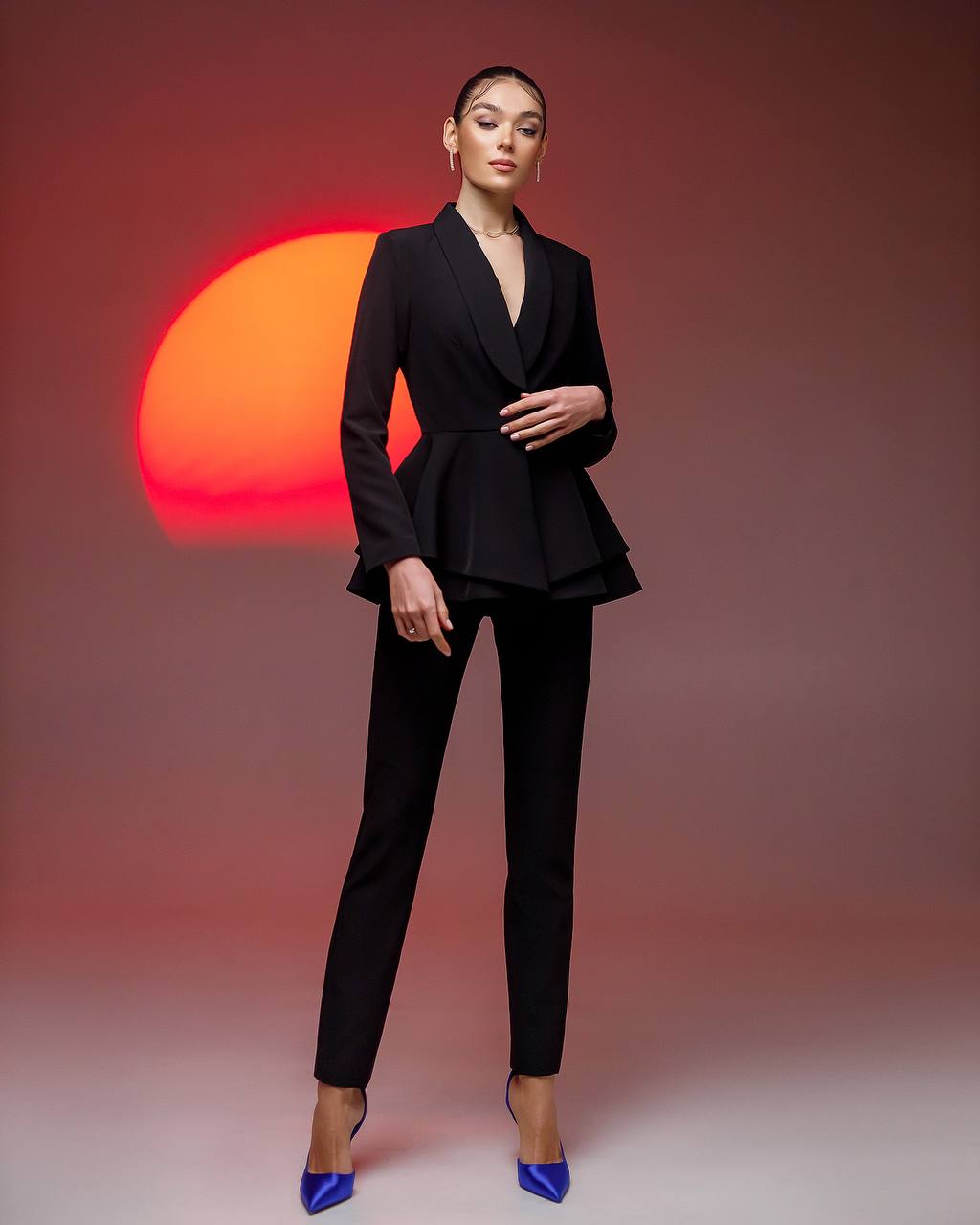 Woman in a black suit standing against a red and orange sunset background