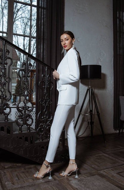 Woman in a white suit standing in an elegant room with decorative elements.