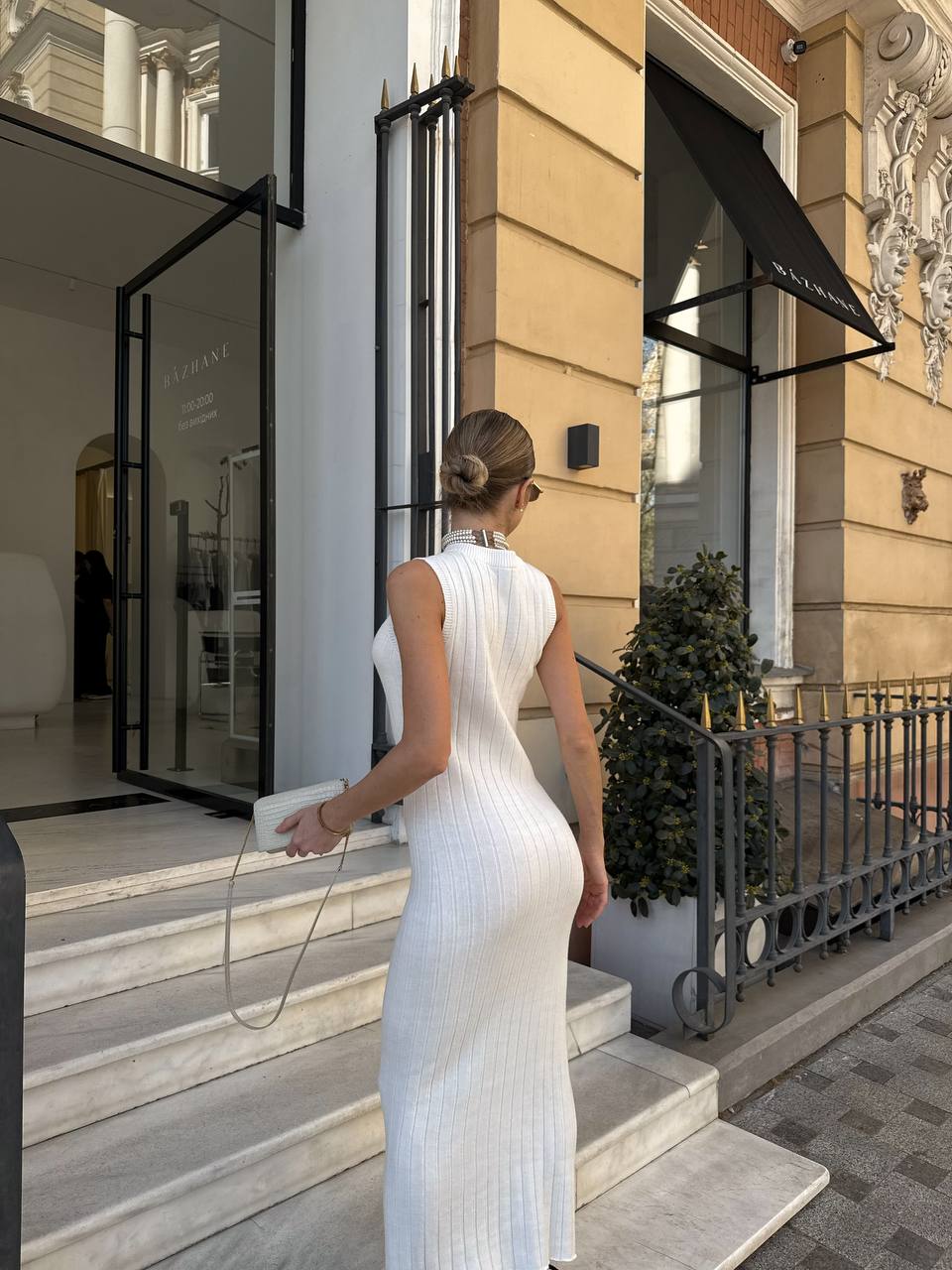 Woman in a white dress entering a building with a stylish exterior.