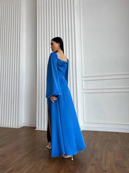 Woman in a blue dress standing against a white paneled wall.