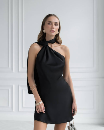 Woman wearing a black one-shoulder dress against a white wall