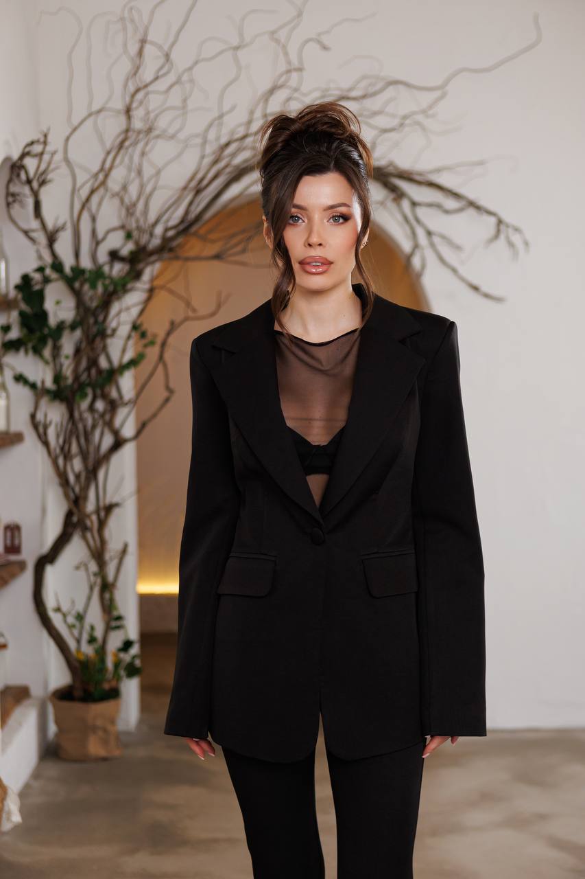 Woman wearing a black suit in an indoor setting with plants and a white wall.