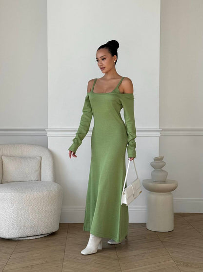Woman in a green dress standing in an elegant room with a white armchair and decorative elements.
