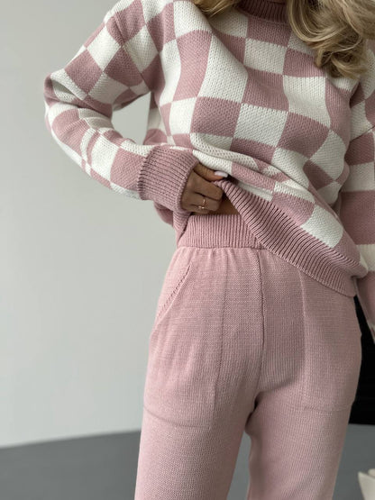 Person wearing a pink and white checkered sweater and matching pants against a plain background