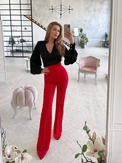 Woman taking a mirror selfie wearing a black top and red pants in a stylish room.