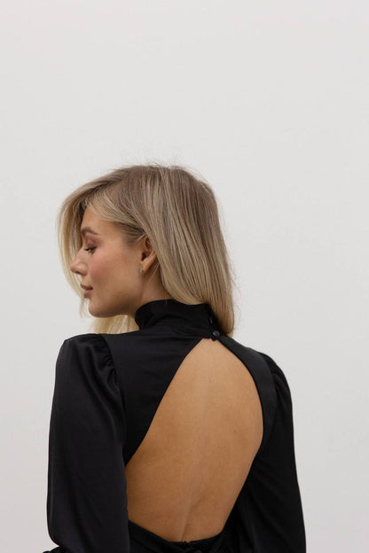 Woman wearing a black open-back top against a white background