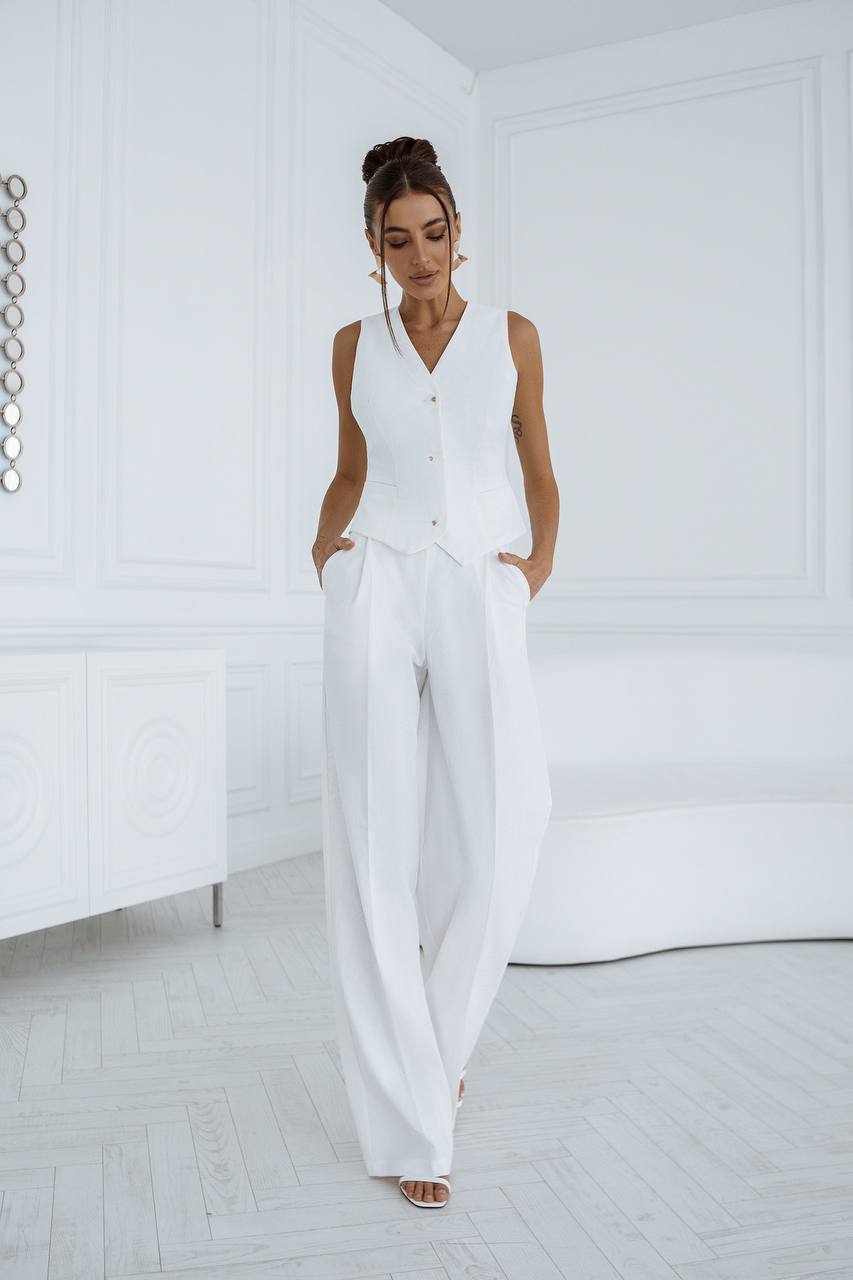 Woman wearing a white sleeveless top and wide-leg pants in a minimalistic room.
