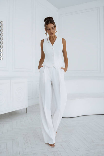 Woman wearing a white sleeveless top and wide-leg pants in a minimalistic room.