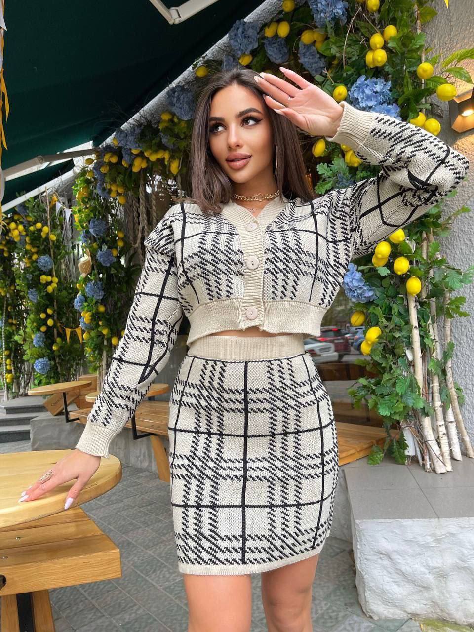 Woman in a black and white checkered outfit standing in front of floral decorations.