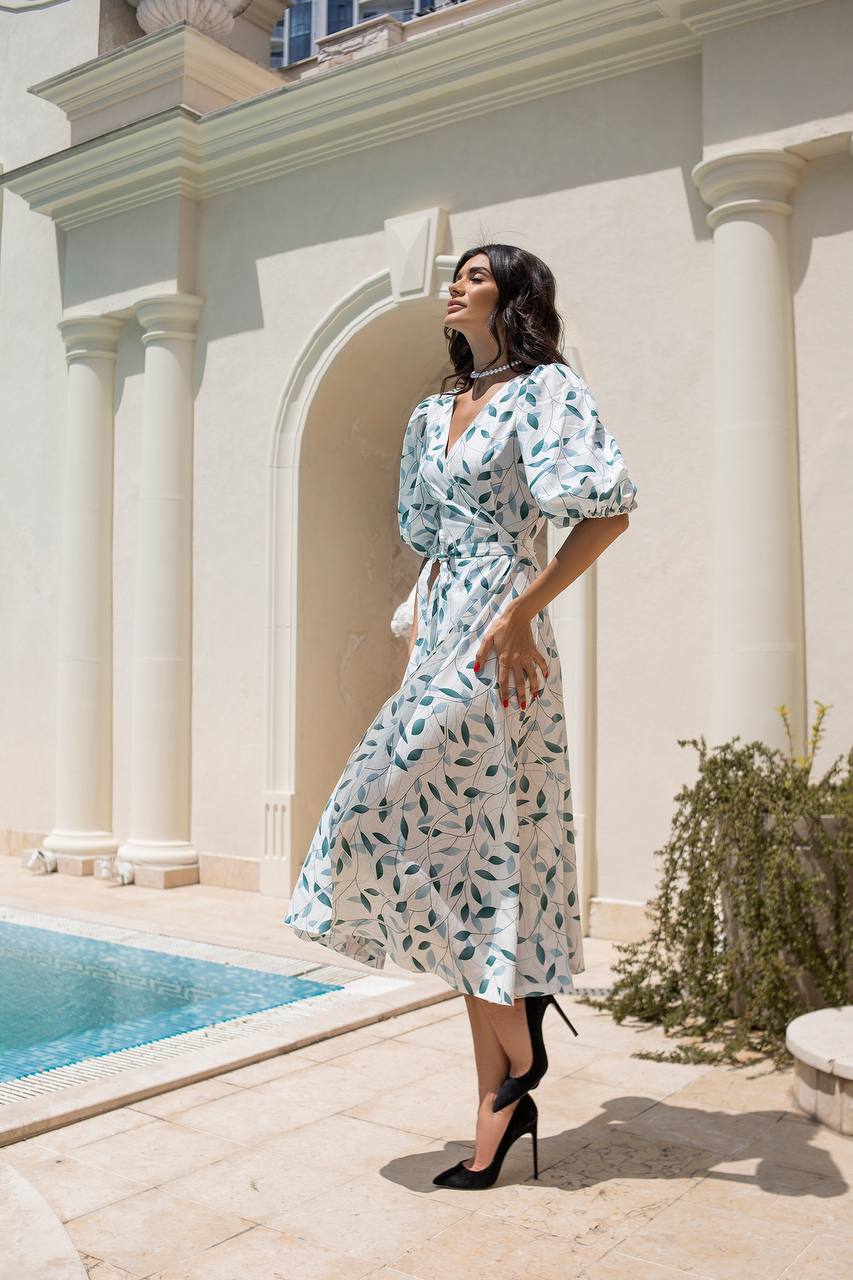 Woman in a floral dress standing by a pool with classical architecture in the background