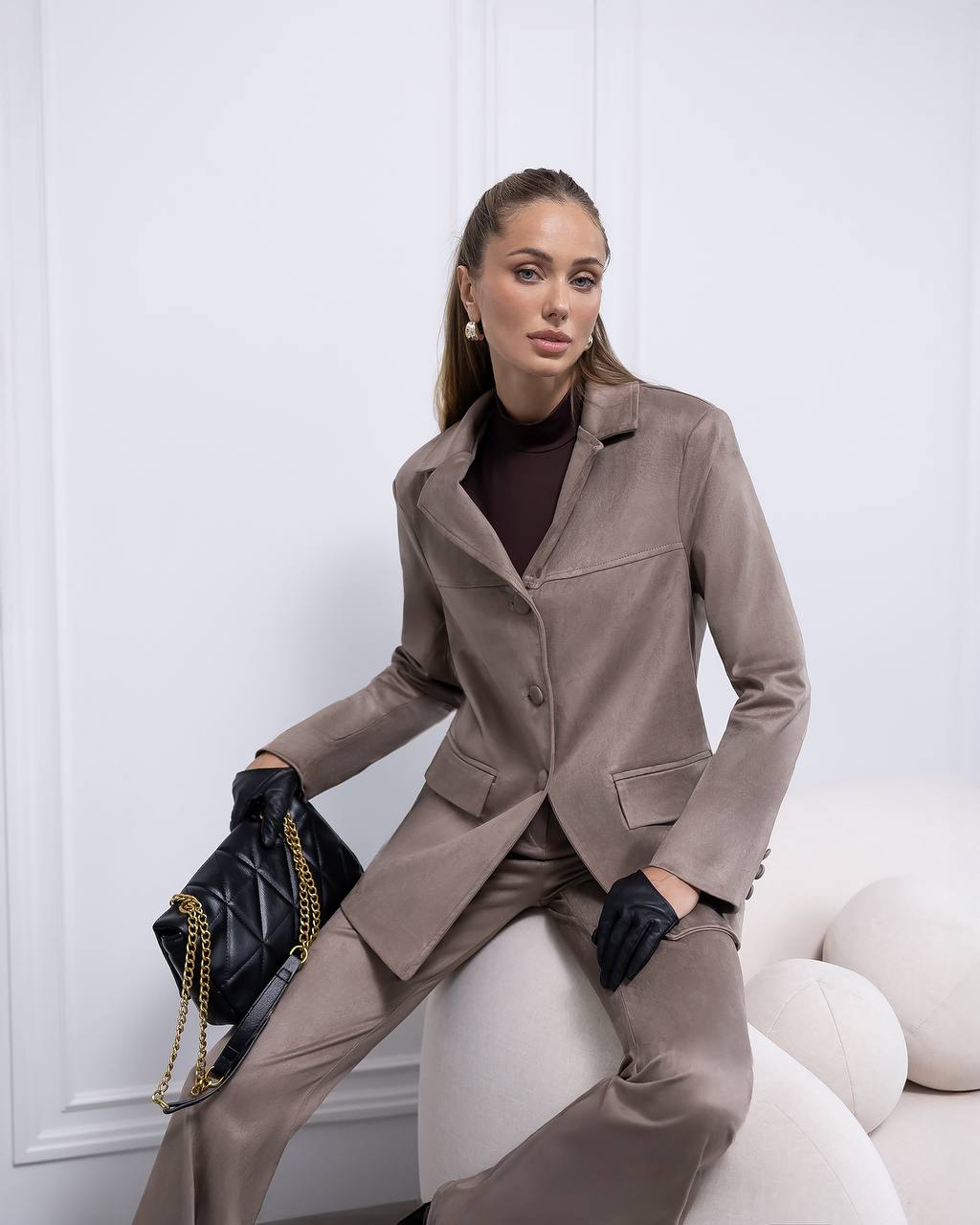 Woman in a beige suit holding a black handbag against a white background