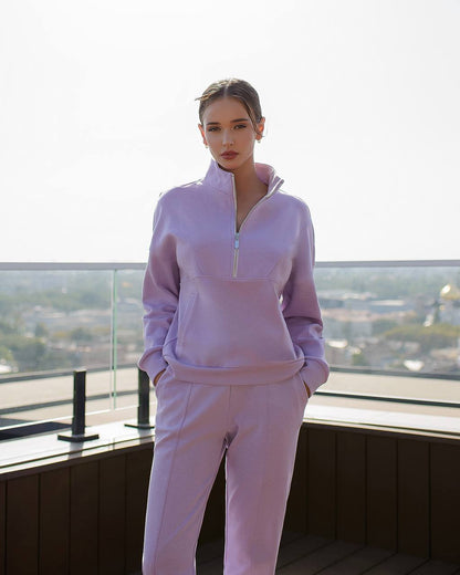 Person wearing a light purple tracksuit standing on a balcony with a cityscape view.