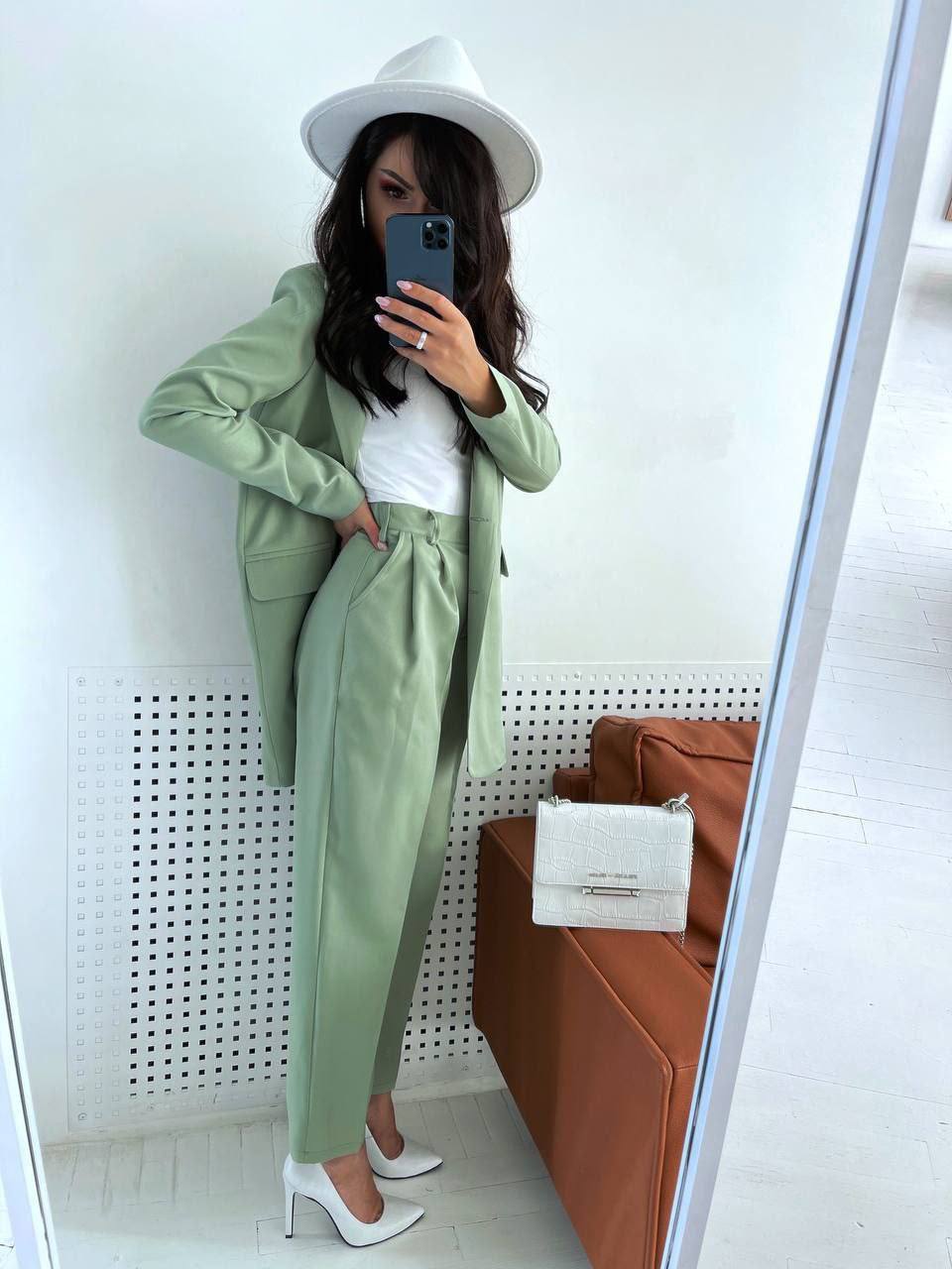 Person wearing a green suit and white hat taking a mirror selfie.