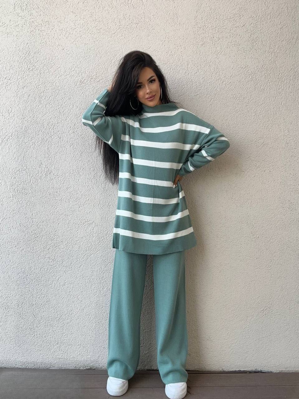 Person wearing a green and white striped sweater and pants against a plain background