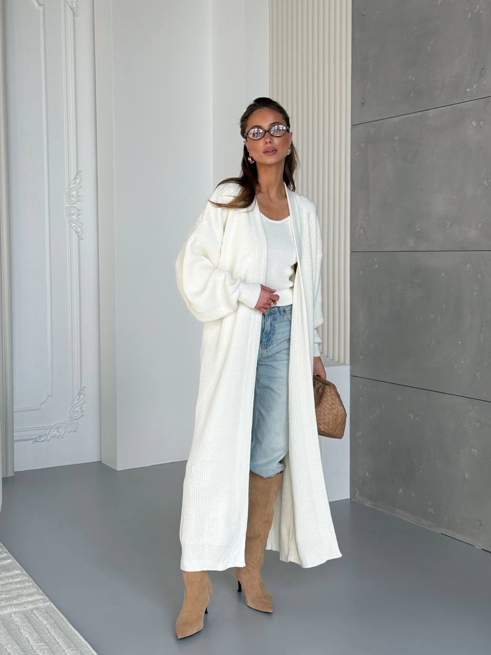 Woman wearing a long white coat, denim shorts, and beige knee-high boots in an indoor setting.
