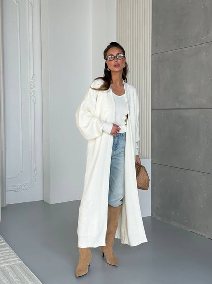 Woman wearing a long white coat, denim shorts, and beige knee-high boots in an indoor setting.