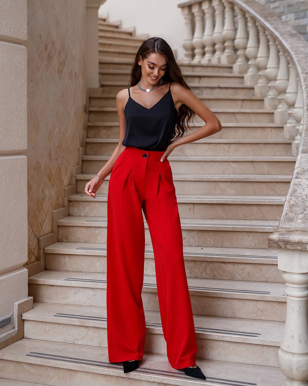 Woman in black top and red pants standing on a marble staircase