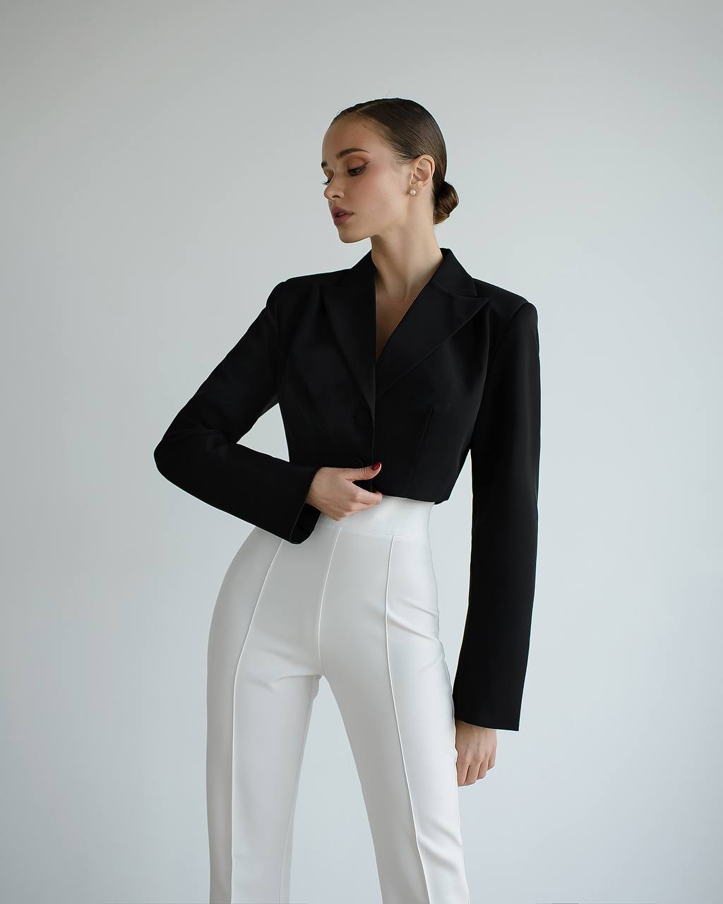 Woman wearing a black blazer and white pants against a plain background