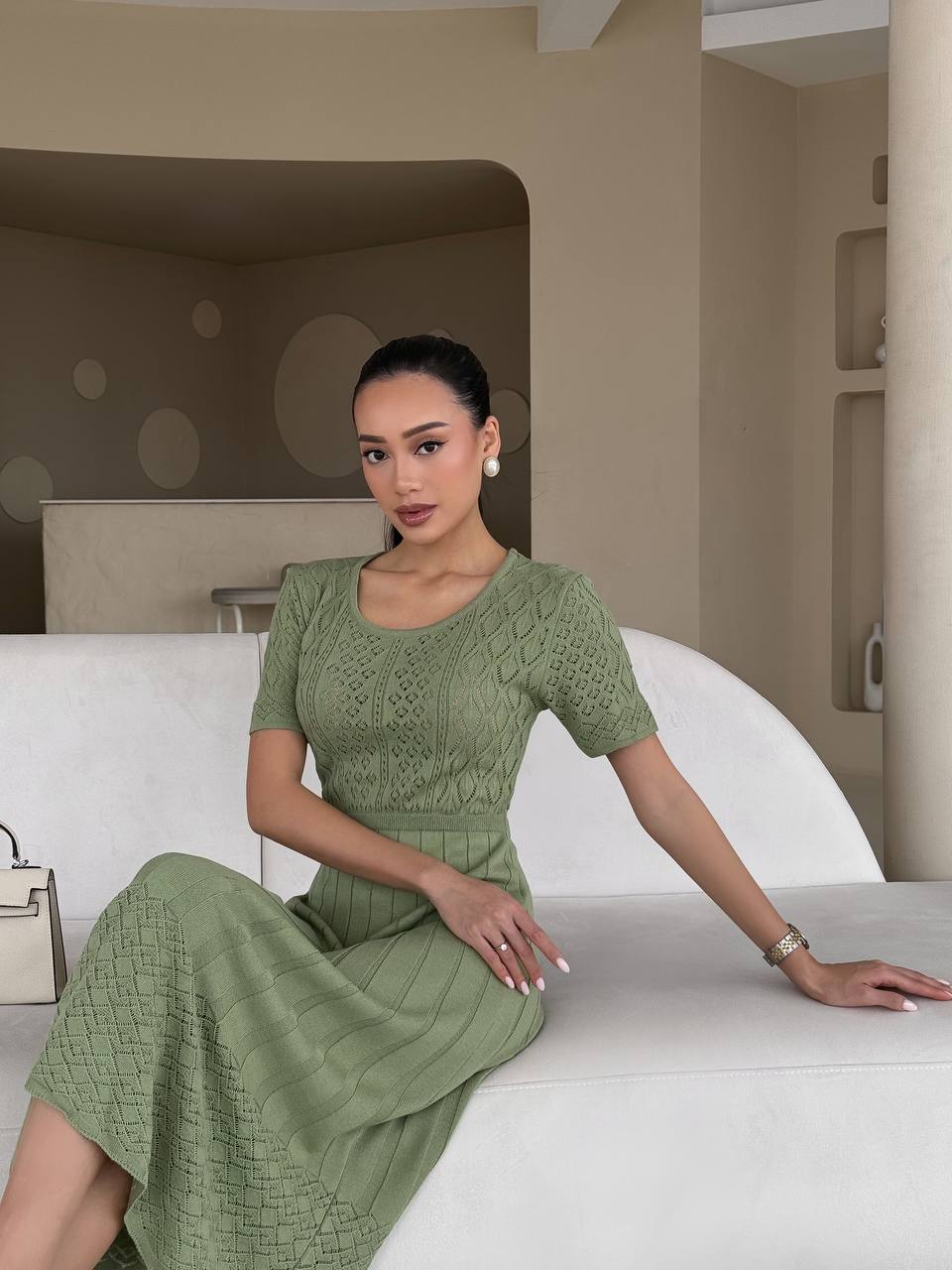 Woman in a green dress sitting on a white couch in a modern interior setting