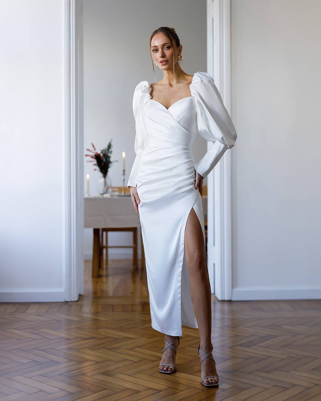 Woman in a white dress standing in a room with a table and decor.