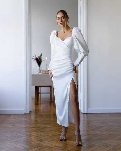 Woman in a white dress standing in a room with a table and decor.