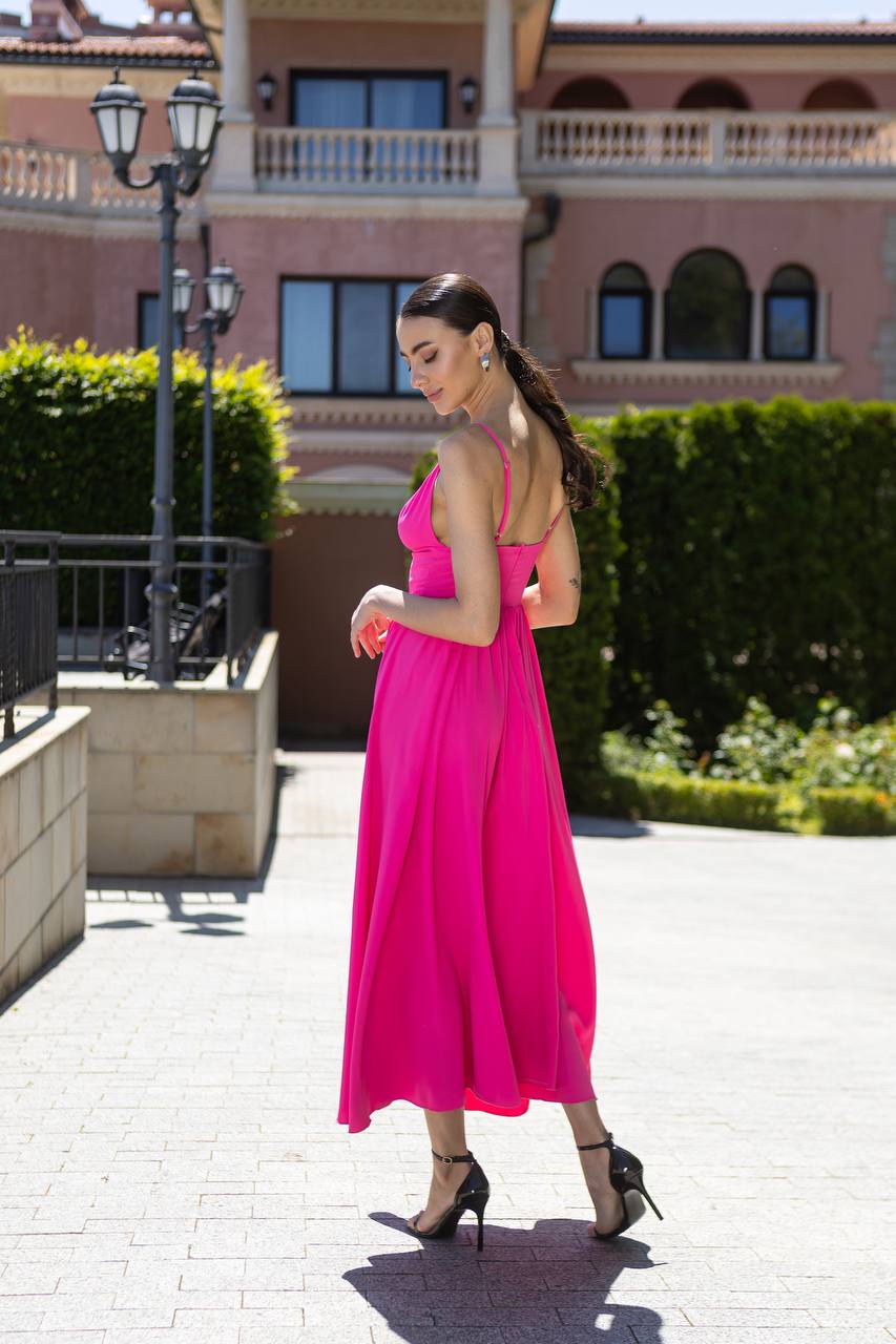 Woman in a pink dress standing on a sidewalk with a building in the background